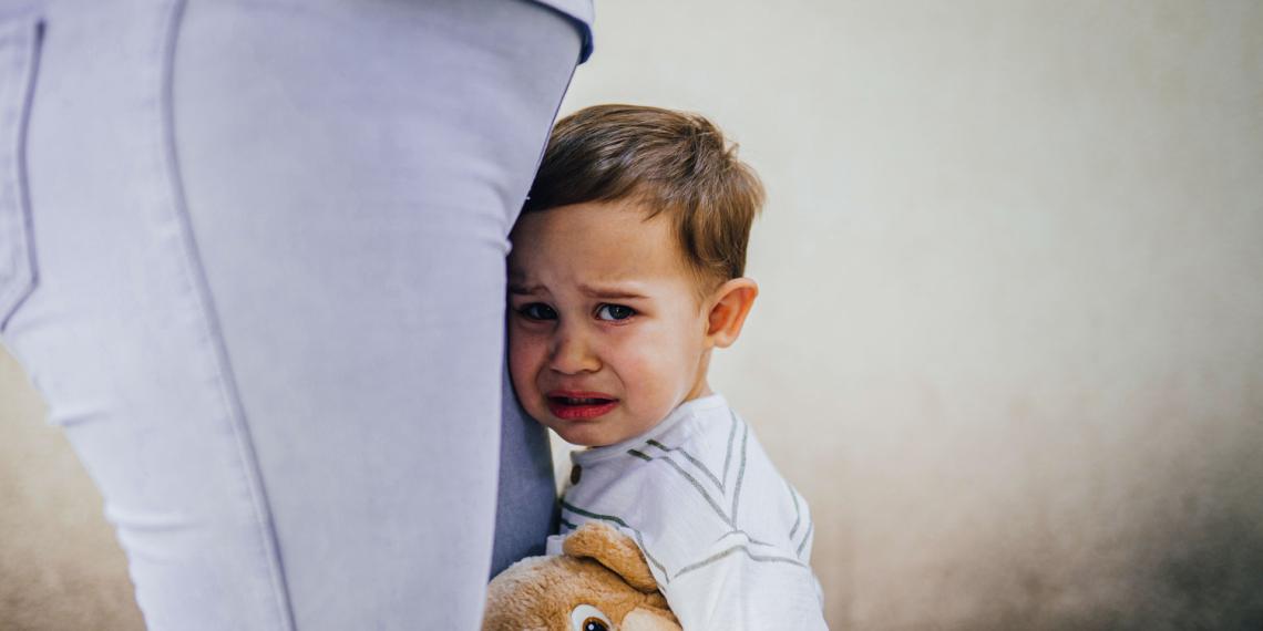 Upset child leaning on his mother's leg holding a soft toy