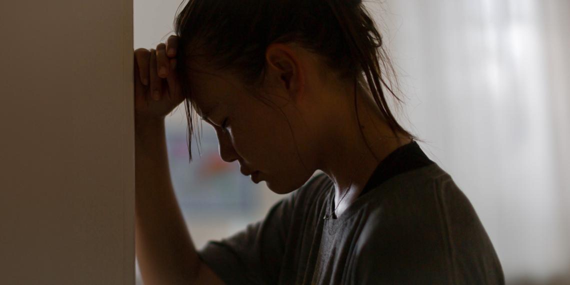 Woman leaning against a door frame looking sad