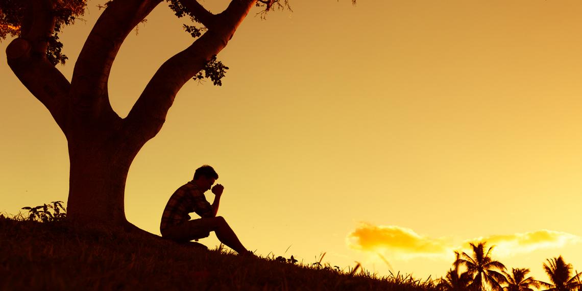 a man sitting under a tree ins a thoughtful pose